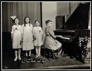Woman playing the piano while three girls sing at the New York Association for the Blind, 111 East 59th Street, New York, c.1917
